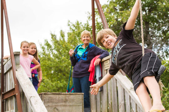 Smiling boy riding the zip line while kids and a grandparent watch from a wooden play structure at Clovermead Adventure Farm