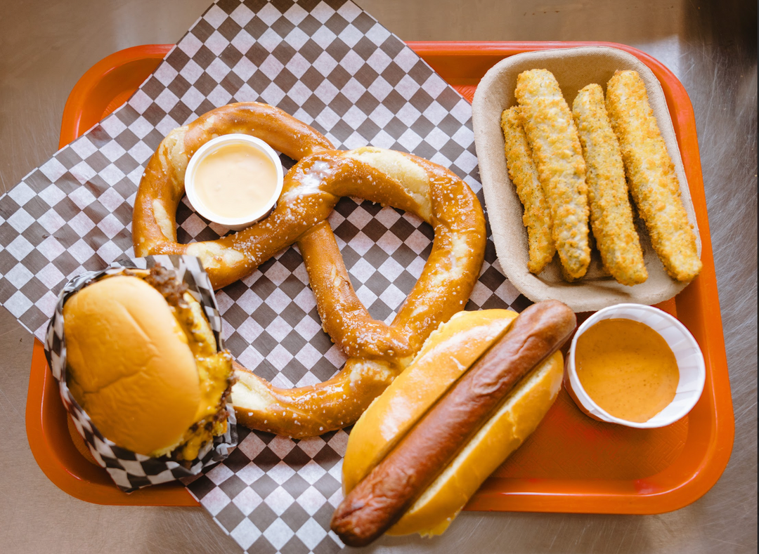 Tray with a smash burger, hot dog, soft pretzel with cheese dip, breaded pickles, and dipping sauces from Clovermead’s Rooster Cookhouse